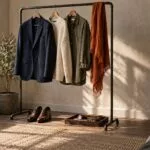 Clothing rack with a navy blazer, cream sweater, olive shirt and orange scarf in soft window light in a photo studio